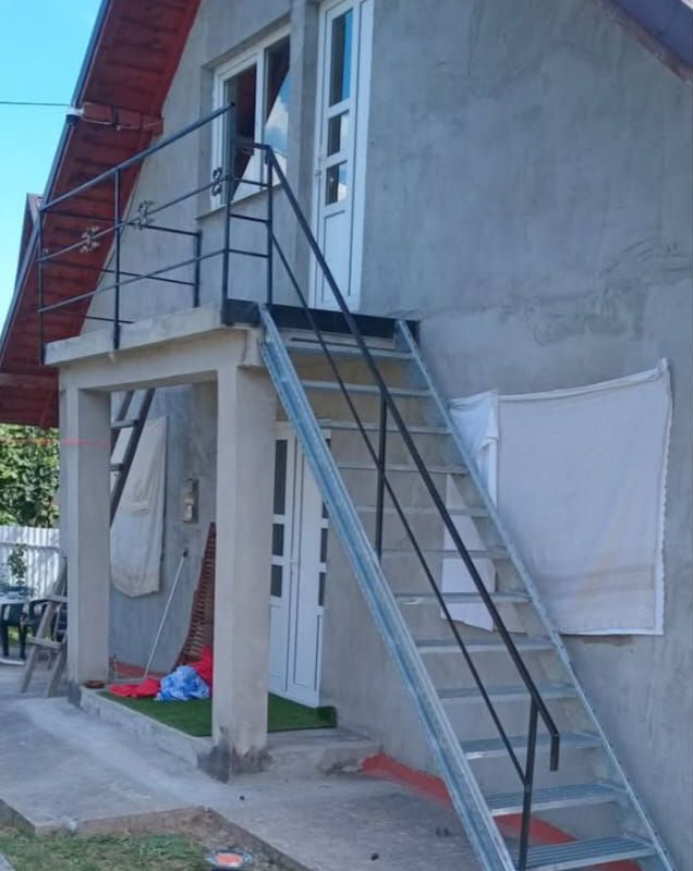 Scară metalică zincată cu mână curentă neagră, care urcă până la un balcon din beton